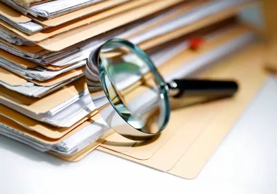 Magnifying glass in front of a stack of files of papers